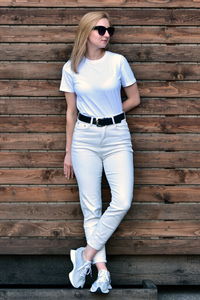 Full length of young woman standing against wooden wall