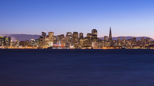 Illuminated buildings in city against clear sky at night