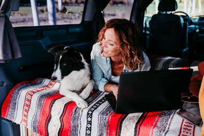 Woman using laptop while lying with dog in camper trailer