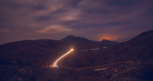 Illuminated road by mountains against sky at night