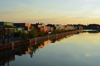 Buildings by river against sky during sunset