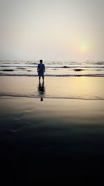 Rear view of man on beach against sky during sunset