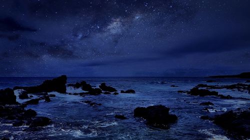 Rocky shore and sea against sky at night