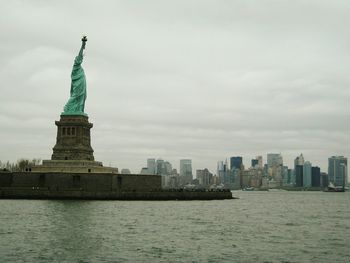 Statue of liberty by hudson river against cloudy sky