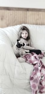 Portrait of girl with dog sitting on sofa at home