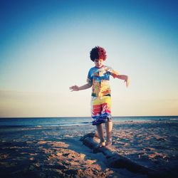 Boy walking at beach against sky during sunset