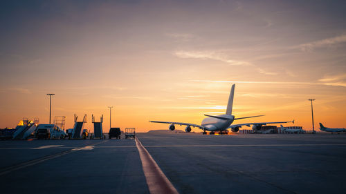 Airplane on airport runway against sky during sunset