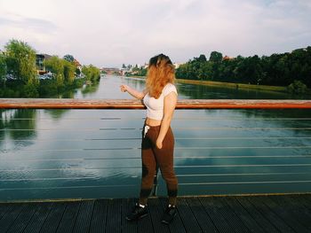 Woman standing by railing against lake against sky