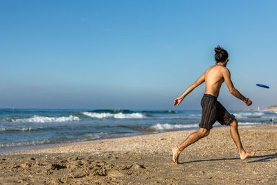 Man playing with disc at beach against sky