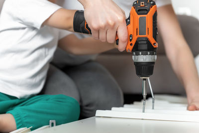 Midsection of mother teaching son to use drill at home