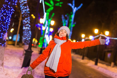 Woman standing against illuminated wall during winter at night