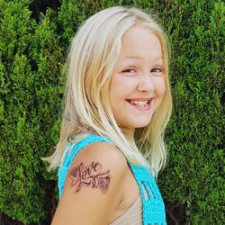 Portrait of smiling girl with tattoo on hand standing against plants