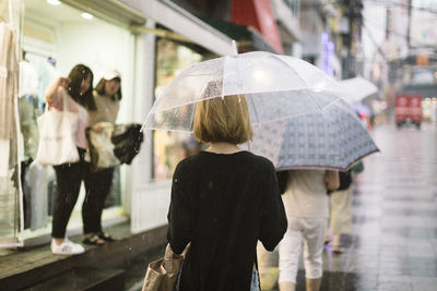 Rear view of woman holding umbrella while walking on street during rainy season