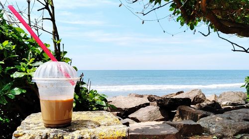 Panoramic shot of drink on rock by sea against sky