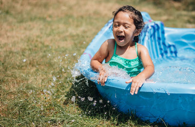 Cute smiling girl sitting in wading pool outdoors