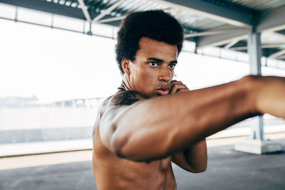 Shirtless male boxer exercising below bridge