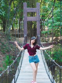 Portrait of woman standing on footbridge in forest