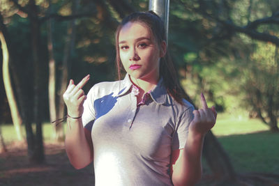 Portrait of beautiful woman showing middle fingers while standing at park