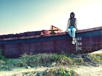 Portrait of young woman standing on grass against clear sky