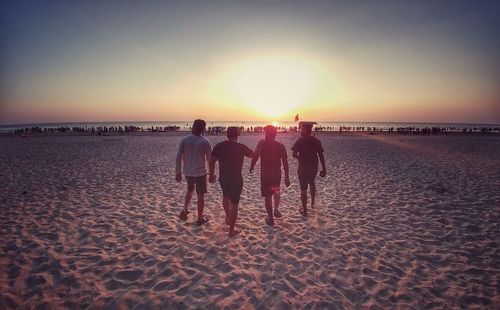 Rear view of people on beach against sky during sunset