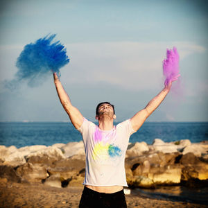 Man playing with powdered paint while standing against sky