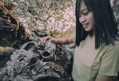 Beautiful young woman standing by tree trunk