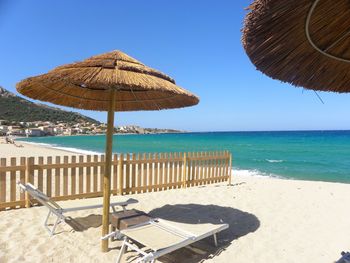 Deck chairs on beach against clear blue sky