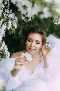 A delicate elegant young woman bride in a wedding dress walks alone in a blooming outdoor park