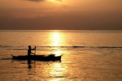 Silhouette man in boat on sea against sky during sunset