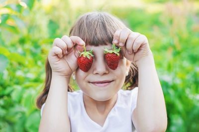 Smiling girl covering eyes with strawberries