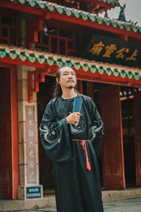 Portrait of young woman standing against building
