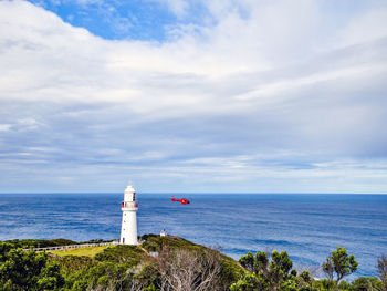 Helicopter flying near lighthouse by sea against sky