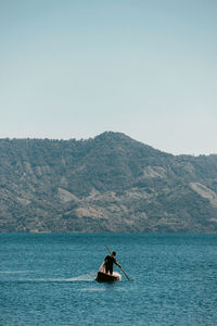 Man rowing boat in sea against mountains