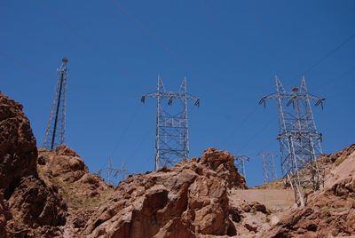 Low angle view of electricity pylons on mountains against sky
