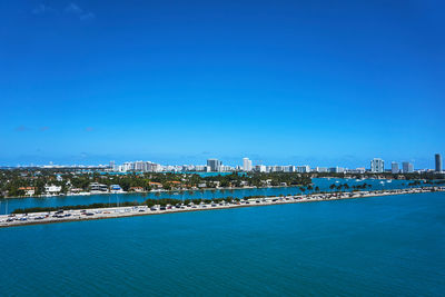 Illuminated city by sea against blue sky