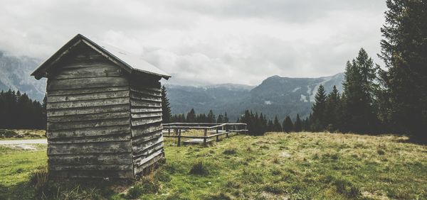View of wooden hut against mountains and cloudy sky