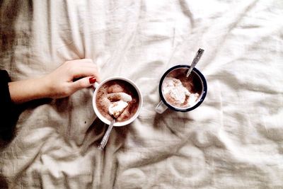 Cropped image of hand holding cup on bed