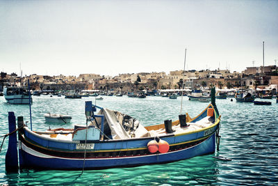 Sailboats moored on sea by buildings against clear sky