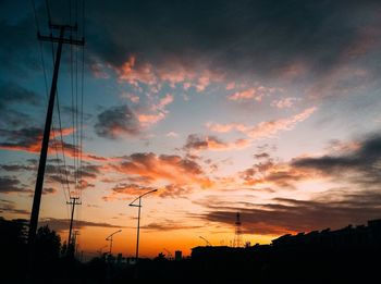 Silhouette electricity pylon against dramatic sky during sunset
