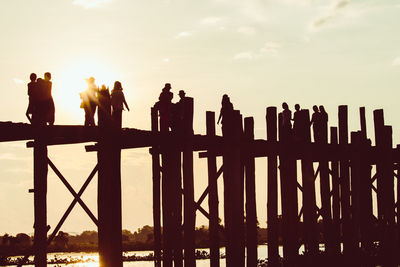 Silhouette people standing by railing against sky during sunset