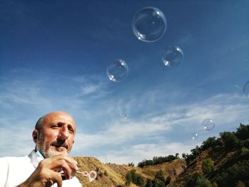 Portrait of man with bubbles against sky