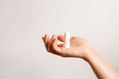 Cropped hand of woman holding pill against white background