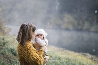 A woman is holding a baby near a river