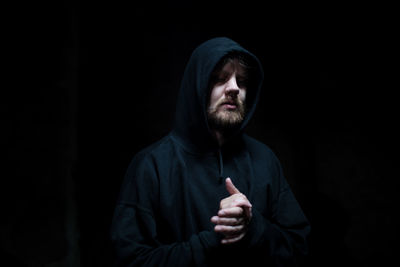 Man with hands clasped against black background