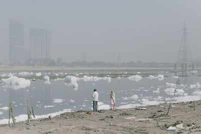 Rear view of people standing on shore against sky