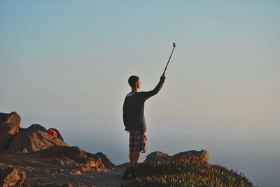 Full length of man taking selfie while standing on mountain against sky