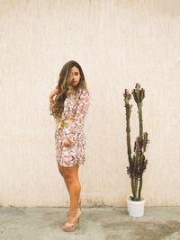 Side view of young woman standing by potted plant against wall
