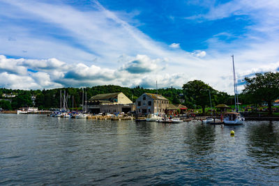 Sailboats in river by houses against sky