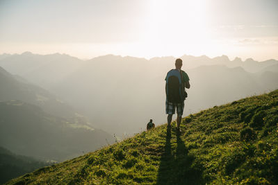 Rear view of male hiker looking at mountains against sky during sunset