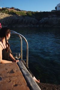 Woman holding wineglass while sitting by river